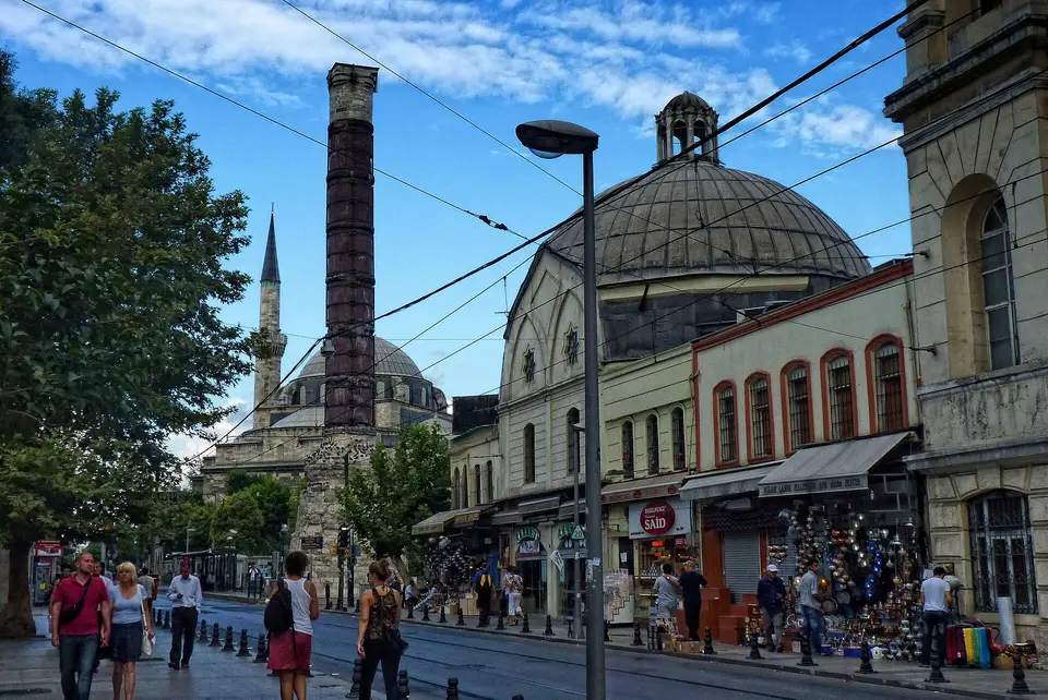 Divanyolu’nda Çemberlitaş Hamamı’nın kubbesi ve önündeki Çemberlitaş sütunu, kaldırımda yürüyen insanlar