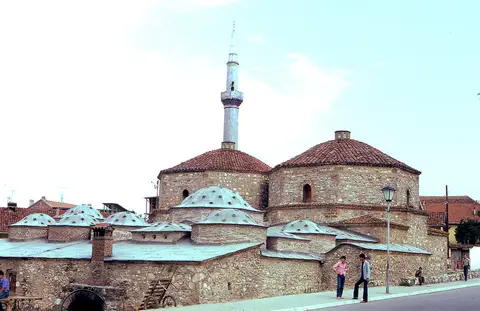 Prizren’de Gazi Mehmed Paşa Hamamı’nın kesme taş gövdesi, kubbeleri ve arkada cami minaresi